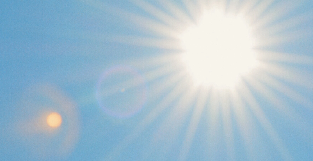 Bright sun shining in a clear blue sky, with lens flare and sun rays visible.