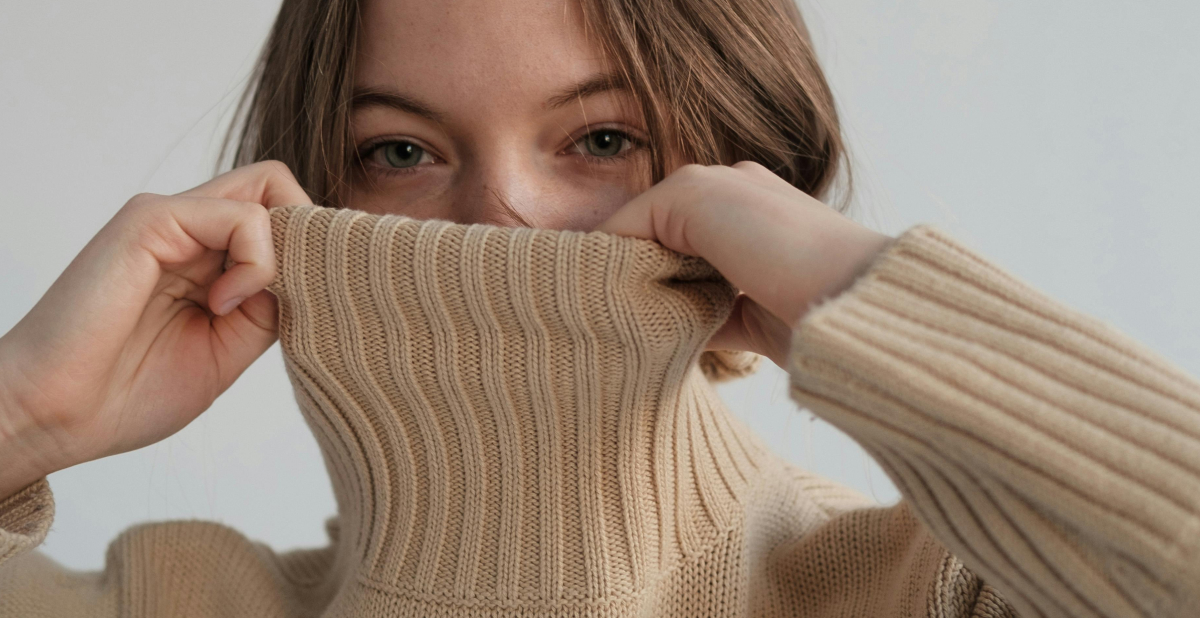 Woman pulling up a knitted sweater to protect her face from cold weather, representing winter skincare protection and hydration